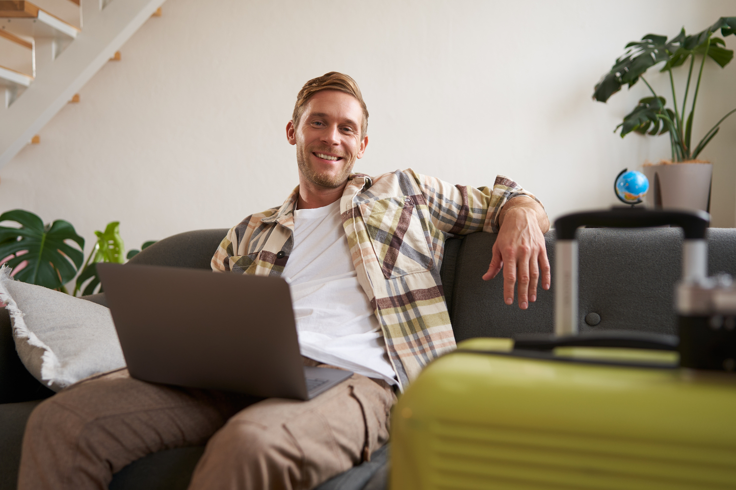 Portrait of happy young man, tourist booking his holiday with travel agency, looking at laptop, packed suitcase to go on vacation